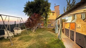 A backyard with a swing set, a tree, a barbecue area, and a stone building. - Alali s Guesthouse With tub (Aalali)