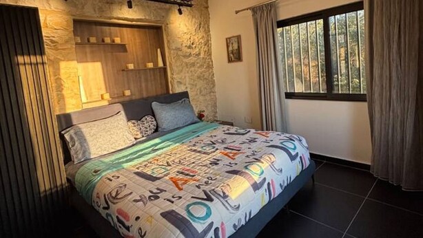 A bedroom with a bed, stone wall, wooden headboard, and a window with curtains. - Alali s Guesthouse With tub (Aalali)