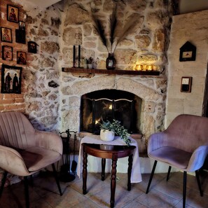 Ein Steinkamin mit Kaminabdeckung, zwei Sessel, ein Tisch mit Pflanze und Bilder an der Wand.