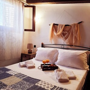 A neatly made bed with pillows, a bedside table with a lamp, a tray with orange juice, and a heart-shaped decoration on the wall. - Traditional Stone House in a Peaceful Cretan Village - 20' from Heraklion Center (Epano Vatheia)