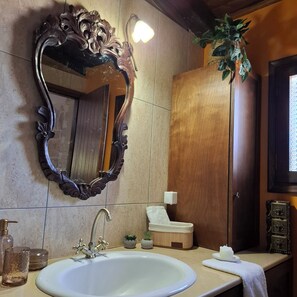 A bathroom with a large ornate mirror, a white sink, a small plant, and a wooden door. - Traditional Stone House in a Peaceful Cretan Village - 20' from Heraklion Center (Epano Vatheia)