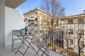 Ein Balkon mit Tisch und Stühlen, Blick auf ein Gebäude mit mehreren Balkonen sowie ein Baum im Hintergrund.