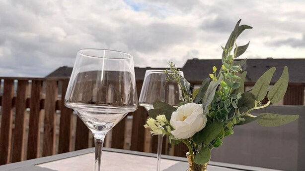 Dos copas de vino sobre una mesa, una vela y un florero con flores.