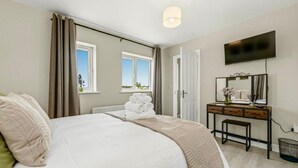 Habitación de hotel con cama, escritorio, televisor y ventana con cortinas.