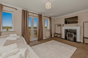 Ein Schlafzimmer mit Bett, Kamin, Blick durch das Fenster und einem Balkon.