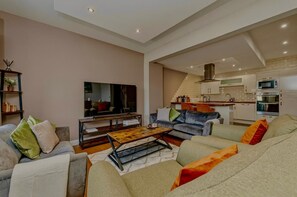 Un salon moderne avec un téléviseur à écran plat, des canapés, une table basse et une cuisine en arrière-plan.