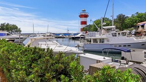 Ein Yachthafen mit vertäuten Booten, ein Leuchtturm im Hintergrund und üppiges Grün im Vordergrund.