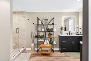 A bathroom with a shower, a wooden bench, a shelf with decorative items, and a dark-colored vanity with a mirror. - Southern charm at its best (Crossville)