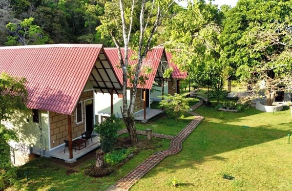 Um pequeno edifício rústico com telhado vermelho, rodeado por um jardim bem cuidado e árvores.