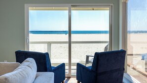Una stanza con un'ampia porta-finestra a vetri scorrevoli che dà su una spiaggia, due sedie blu e un divano bianco.