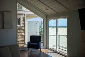 A room with a large sliding glass door leading to a beach view, a chair, and a bookshelf.