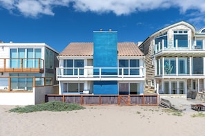 Une propriété située en bord de mer, caractérisée par une structure verticale bleue imposante, un balcon et un patio couvert.
