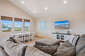 A living room with a large window, a flat-screen TV, a dining area, and a sofa. - One More Cast 3 Bedroom Home (Port Bolivar)