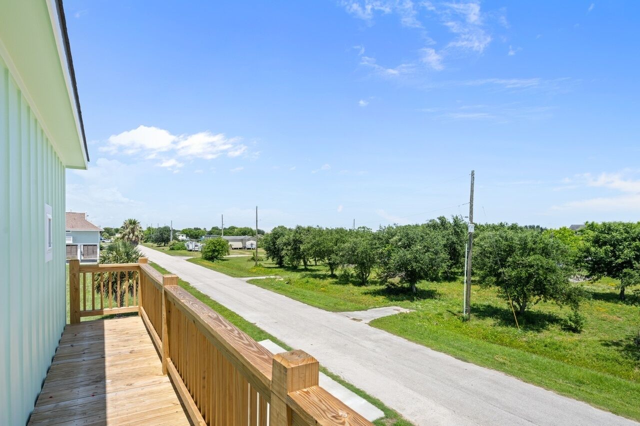 A residential property with a wooden deck, a clear road, and an orchard in the background.