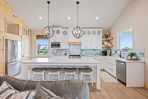 A modern kitchen with a central island, white cabinetry, and a view to the outdoors. - One More Cast 3 Bedroom Home (Port Bolivar)