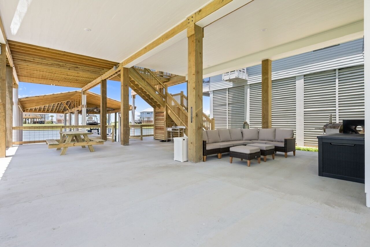 An open-plan living area with a wooden staircase, outdoor seating, and a view of the water.