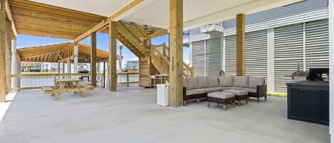 An open-plan living area with a wooden staircase, outdoor seating, and a view of the water.