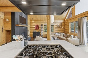 A log cabin interior with a kitchen area, a fireplace, a sofa, and a dining table. - Log Cabin With Shou Sugi Ban Fireplace - Vh401 4 Bedroom Home (Arnold)
