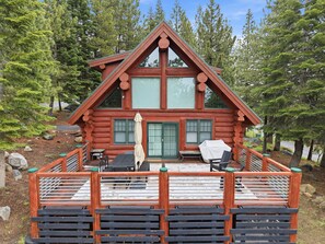 A log cabin with a deck, outdoor seating, and a view of the surrounding forest. - Log Cabin With Shou Sugi Ban Fireplace - Vh401 4 Bedroom Home (Arnold)