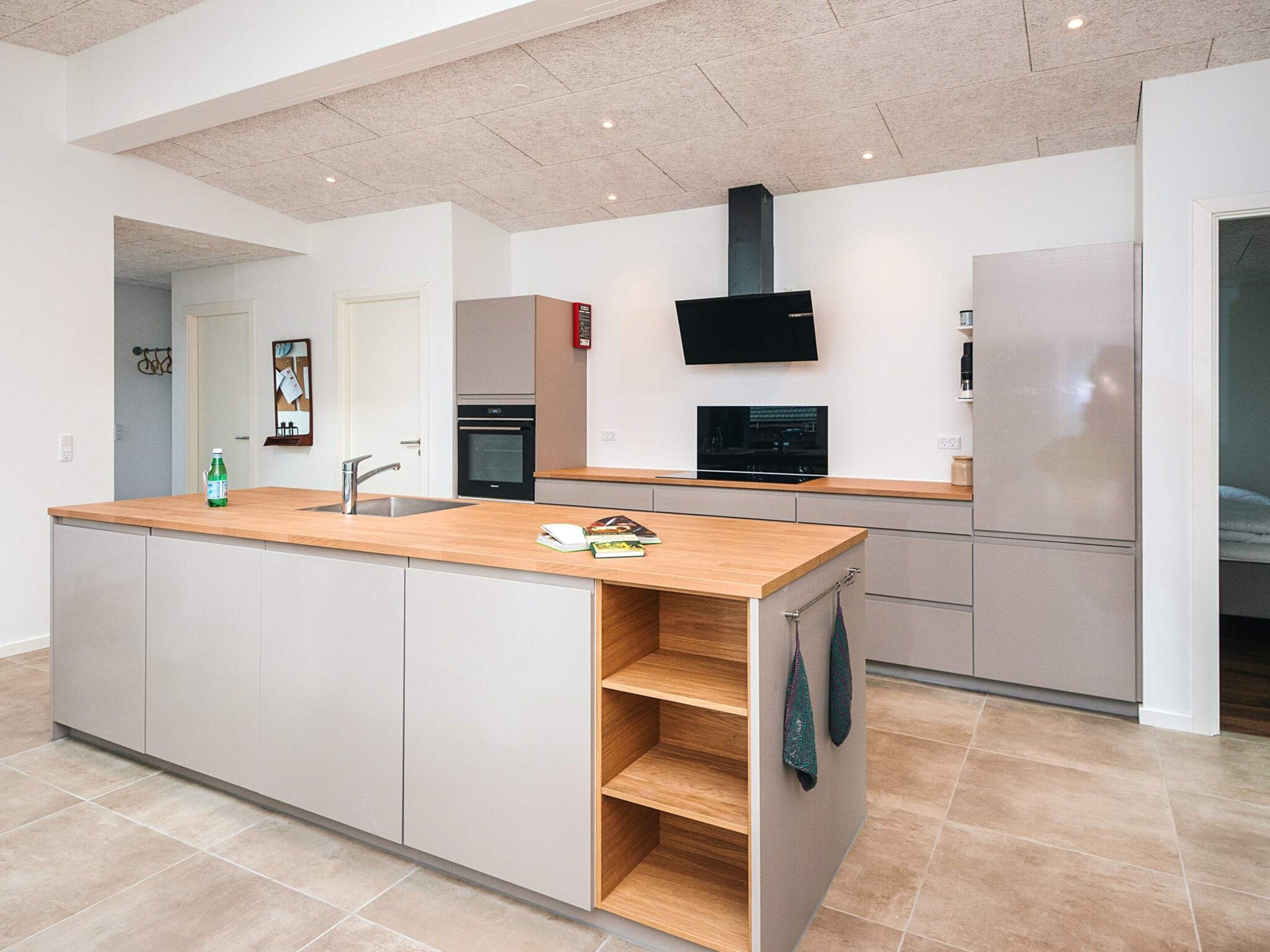 A modern kitchen with a central island, built-in oven, and a flat-screen TV.