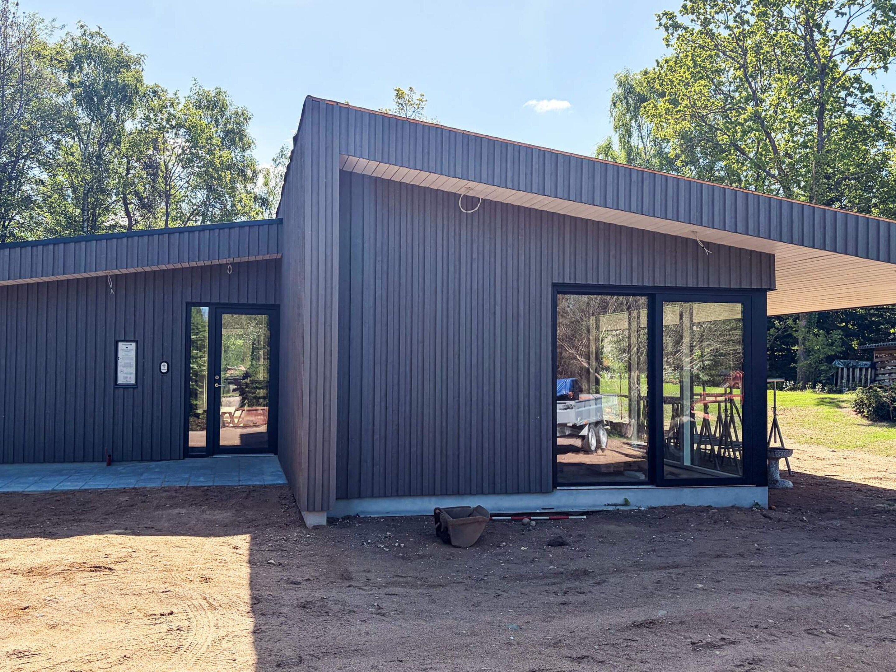 Een modern gebouw met een metalen gevel, grote schuifdeuren en een overdekt buitengebied.