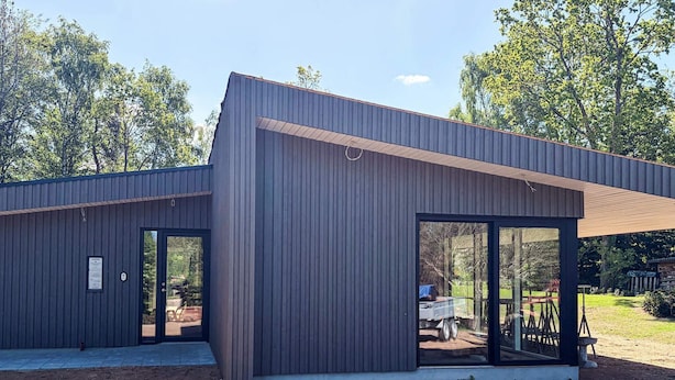 Un edificio moderno con fachada metálica, puertas de cristal grandes y un espacio exterior cubierto.