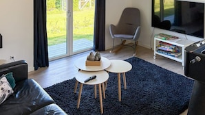 Un salón con sofá, dos mesitas, televisor y estantería con juegos de mesa.