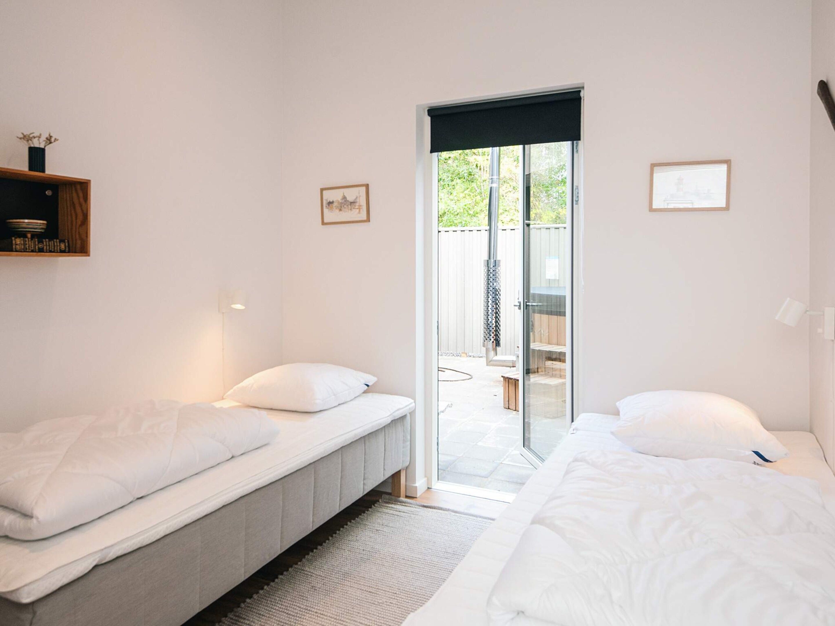 A bedroom with two beds, a sliding glass door leading to an outdoor area, and a small shelf with decorative items.