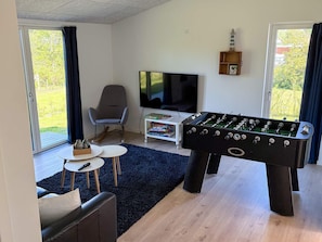Ett vardagsrum med ett fotbollsspel, en tv, en fåtölj och en bokhylla.