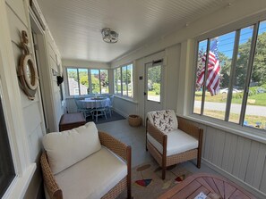 A covered porch with wicker furniture, a table, and chairs, and a view of the neighborhood. - 4-bedroom Charming Cape Cod Cottage (Falmouth)