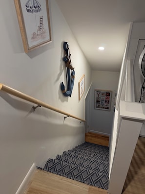A staircase with a wooden handrail, a patterned rug, and wall-mounted decorations including a framed picture and a nautical-themed wall hanging. - 4-bedroom Charming Cape Cod Cottage (Falmouth)