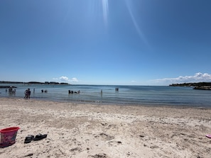 A beach with clear skies, calm water, and footprints in the sand.
