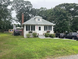 A single-story house with a front porch, a chimney, and a flag.