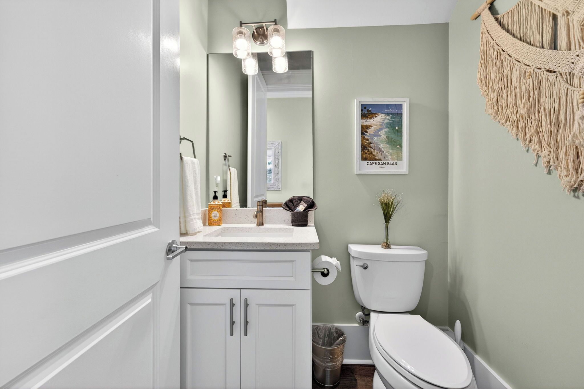 A bathroom with a toilet, sink, mirror, and a framed picture on the wall.