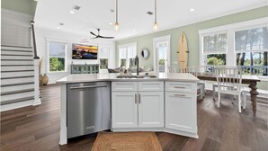 A modern kitchen with white cabinetry, a stainless steel dishwasher, and a dining area with a wooden table and white chairs. - Gulf View Pool | Deeded Beach Access | Jubilation | Sleeps 11, Boat Parking (Pot St Joe)