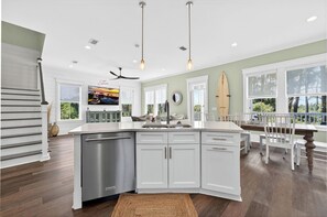 Une cuisine moderne avec des meubles blancs, un lave-vaisselle en acier inoxydable et un coin repas comprenant une table en bois et des chaises blanches.