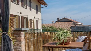 Une terrasse avec une table et des chaises, un pot de fleurs et une vue sur un immeuble doté de fenêtres et de volets.