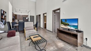 A modern living room with a flat-screen TV, a sofa, a coffee table, and a dining area with chairs and a kitchen in the background. - 2 Bd Loft 603 @ Playa. Pool & Hot Tub (Kelowna)