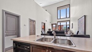 A modern kitchen with a large island, built-in dishwasher, and a dining area with black chairs. - 2 Bd Loft 603 @ Playa. Pool & Hot Tub (Kelowna)