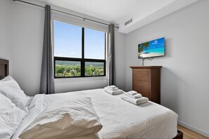 Ein Schlafzimmer mit Bett, Fenster mit Blick, einem hölzernen Schminktisch und einem Bild an der Wand.