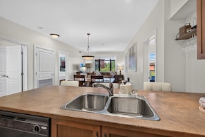 A kitchen with a double sink, wooden cabinets, and a dining area with a table and chairs. - Bright 3 Bd at Playa 548. Pool & 1 min to Beach (Kelowna)