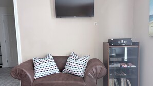 A brown leather sofa with patterned pillows, a flat-screen TV on the wall, and a record player cabinet. - Bayside Coastal Retreat Near Copano Bay (Bayside)