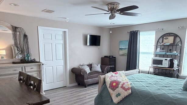 A bedroom with a bed, a desk, a chair, a sofa, a television, a ceiling fan, and a window with curtains. - Bayside Coastal Retreat Near Copano Bay (Bayside)