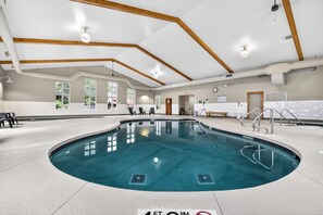 Une piscine intérieure avec une profondeur d’eau de 1,2 mètre à l’entrée, des poutres en bois au plafond et de grandes fenêtres.