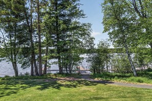 A pathway leading to a dock by a lake, surrounded by tall trees and grassy areas.