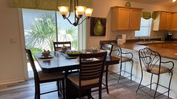 A dining area with a table set for four, a chandelier, and wooden cabinets. - Cozy Collier Retreat with Fire Pit, Dog Friendly Near Brownwood (The Villages)