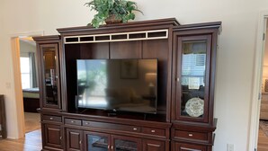 A dark wood entertainment center with a flat-screen TV, glass-fronted cabinets, and a decorative plant on top. - Cozy Collier Retreat with Fire Pit, Dog Friendly Near Brownwood (The Villages)