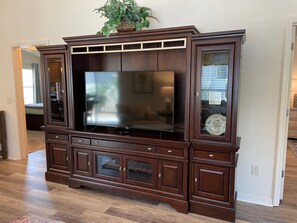 A dark wood entertainment center with a flat-screen TV, glass-fronted cabinets, and a decorative plant on top. - Cozy Collier Retreat with Fire Pit, Dog Friendly Near Brownwood (The Villages)
