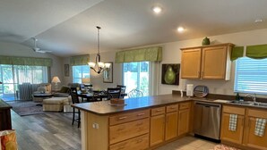 A kitchen with a central island, wooden cabinets, a dishwasher, and a dining area with chairs and a table. - Cozy Collier Retreat with Fire Pit, Dog Friendly Near Brownwood (The Villages)