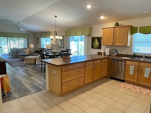 A kitchen with a central island, wooden cabinets, a dishwasher, and a dining area with chairs and a table. - Cozy Collier Retreat with Fire Pit, Dog Friendly Near Brownwood (The Villages)